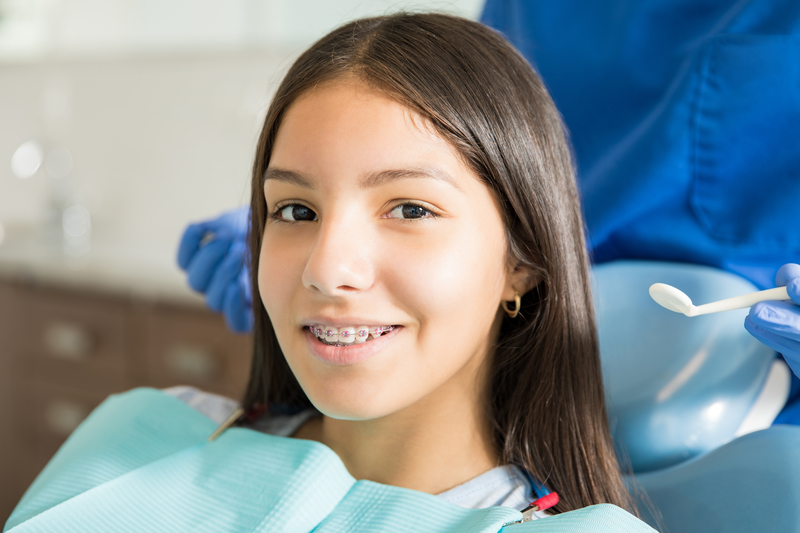 Young woman with braces on her teeth that is sitting in a dental chair getting dental services.