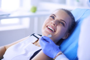 A young adult woman sitting in an orthodontic chair smiling at the hygienist.