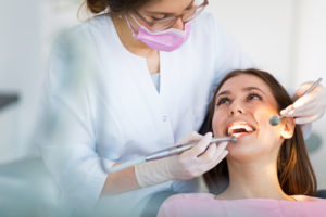 A young adult woman that is having her teeth looked at by a dental hygienist. She is looking up at the hygienist as she does her exam. 