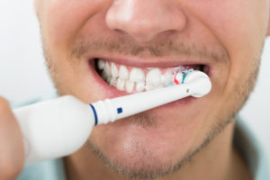 Smiling man brushing teeth with an electric toothbrush
