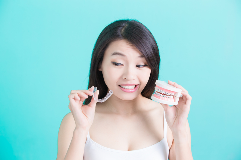 Woman holding Invisalign retainer in one hand with an impression of a mouth in the the other