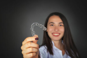 Young woman smiling while holding an Invisalign aligner in front of her