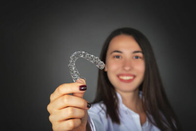 Young woman smiling while holding an Invisalign aligner in front of her